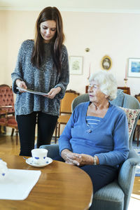 Young woman holding magazine by grandmother in living room