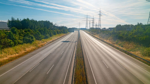 Road by electricity pylon against sky