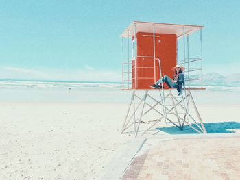 Full length of woman wearing hat sitting on lifeguard hut