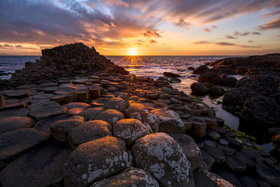 Rocks on sea shore against sky during sunset