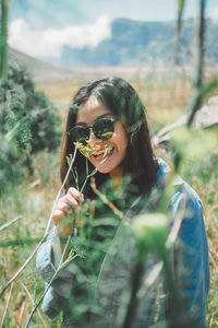 Portrait of young woman holding plant on field