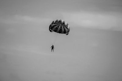 Low angle view of people paragliding against sky