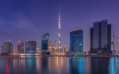 Lake against illuminated burj khalifa in city at dusk