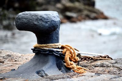 Rope and rusty chain tied to bollard on pier