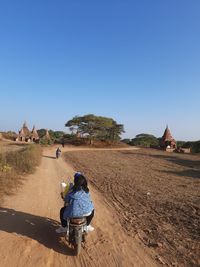 Rear view of man riding motorcycle on field against clear sky