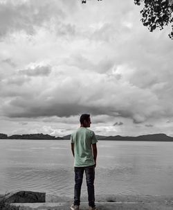 Rear view of man standing by lake against sky