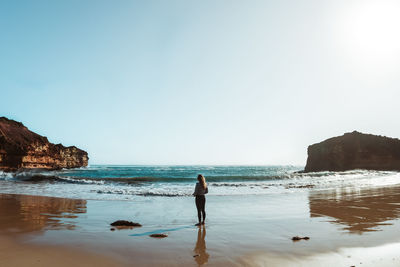 Woman standing on cliff by sea against clear sky