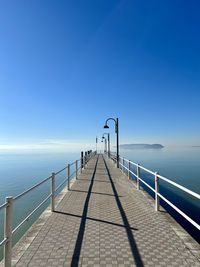 Pier over sea against clear blue sky