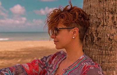 Smiling young woman standing at beach against sky