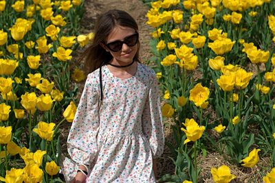 Portrait of smiling young woman standing by yellow flower