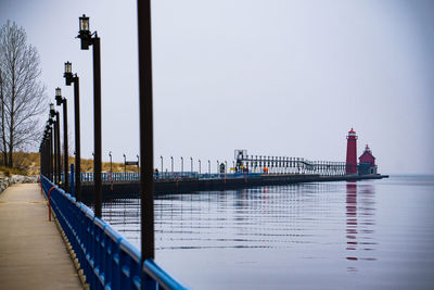 Pier leading towards lighthouse by lake against sky