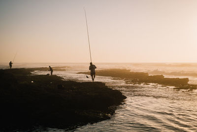 Men fishing in sea against sky