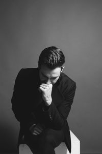 Portrait of young man sitting against wall