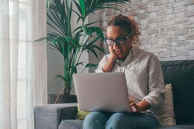 Young woman using laptop while sitting on sofa at home