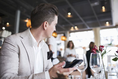 Businessman looking away while holding mobile phone at restaurant