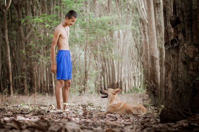 Shirtless teenage boy with dog in forest