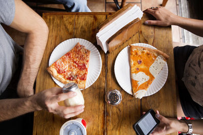 Midsection of friends having pizza at wooden table in restaurant