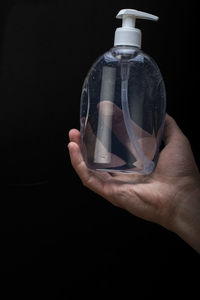 Close-up of hand holding glass bottle against black background