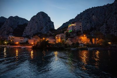 Illuminated buildings under rock formations at dusk on the sea in omis, croatia.