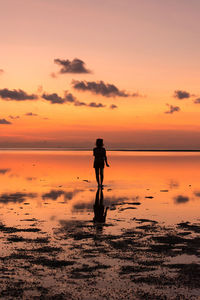 Woman walking at beach against sky during sunset