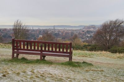 Empty bench on field against sky