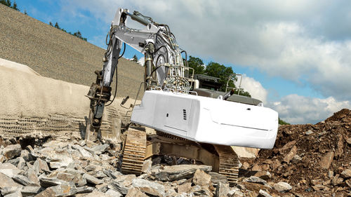 A white excavator offers space for own text. it chisels rocks with hydraulic hammer. highway 