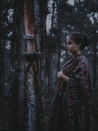 Woman standing by tree trunk in forest