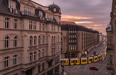 Cable car on city street amidst buildings against cloudy sky at sunset