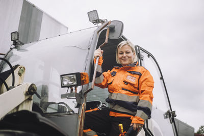 Portrait of smiling female construction worker standing at doorway of vehicle