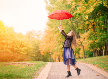 Full length of young woman with umbrella standing on field