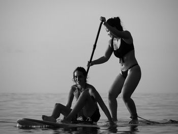 2 young women paddle boarding on sea against clear sky