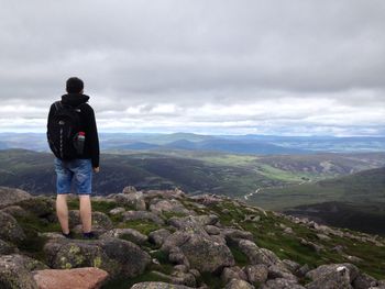 Rear view of hiker standing on mountain against sky