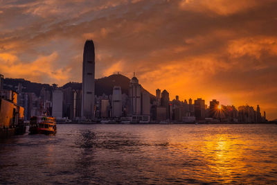 Sea by buildings against sky during sunset