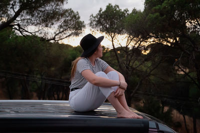 Woman sitting on railing against trees