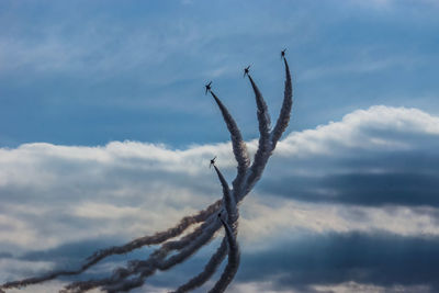 Low angle view of airplanes performing airshow in cloudy sky