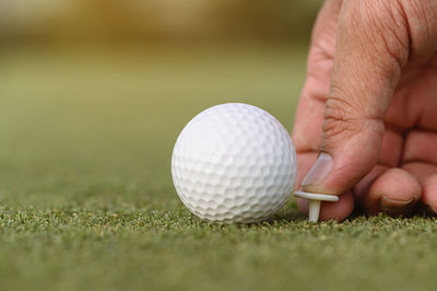 Close-up of hand holding golf ball on land