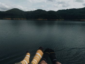 Low section of person by lake against sky