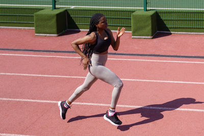 Young woman in headphones runs every day on red track at sports ground of big residential complex