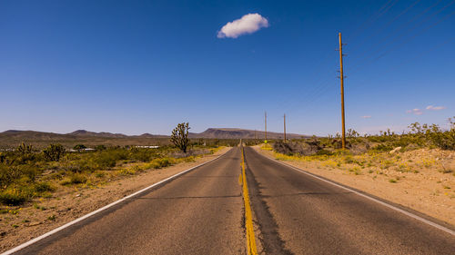 Empty road by landscape against blue sky