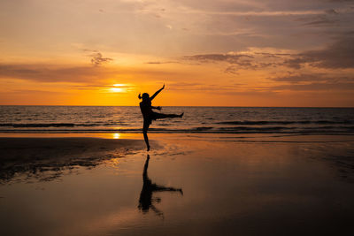 Silhouette of woman jumping on beach at sunset