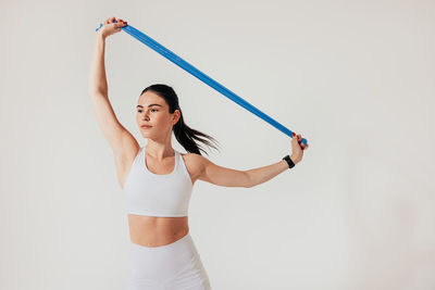 Young woman exercising with arms raised standing against white background