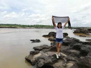 Full length of woman standing on rock at sea shore against sky