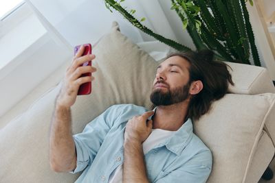 Young man using mobile phone while sitting on bed at home