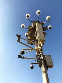 Low angle view of floodlights and security camera against clear blue sky