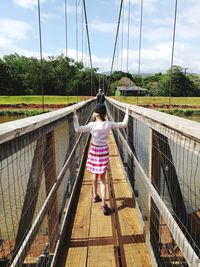Rear view of girl walking on footbridge over river against sky