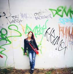 Full length of young woman standing against graffiti wall