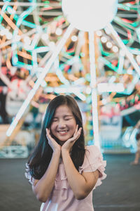 Smiling young woman standing at amusement park during night