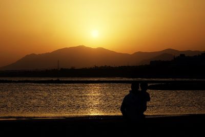 Rear view of silhouette man by lake against sunset sky