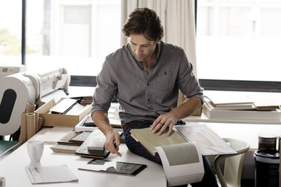 Interior designer using tablet computer while analyzing fabric swatches at desk in office