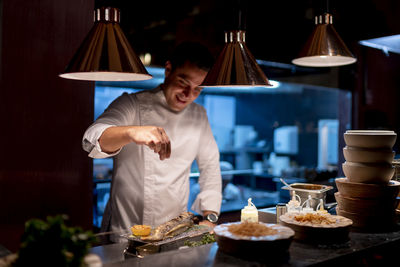 Male chef sprinkling seasoning seafood in kitchen at restaurant